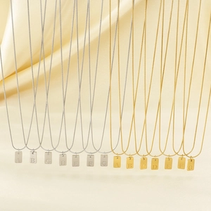 Minimalistische vierkante letter hanger ketting in goud en zilver op zijden achtergrond
