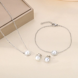 Détail de parure bijoux en acier titane argenté avec perles blanches sur fond de soie