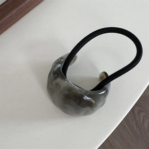 Detail of translucent grey-green resin ring with black elastic hair tie on a desk