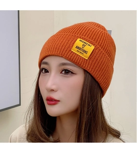 Close-up of orange knit beanie texture and yellow fabric patch with black letter text