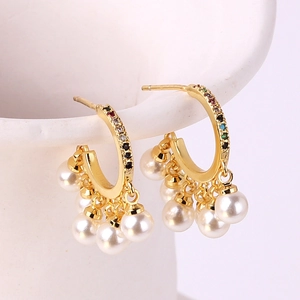 Vintage pearl tassel hoop earrings with colorful gemstones hanging on a white ceramic cup