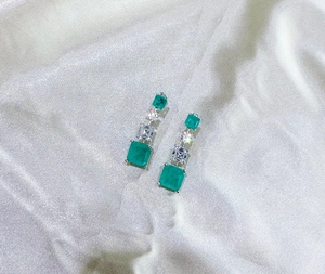 Detail of emerald cut synthetic green gemstone earrings on white silk fabric background