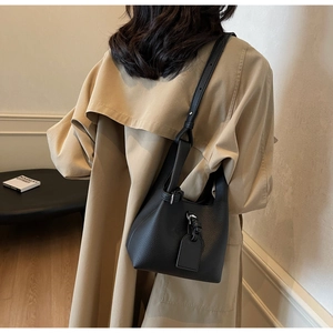 Detail of black lychee grain bucket bag worn with a khaki trench coat and shoulder strap