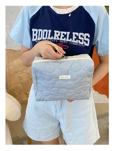 Trousse de maquillage matelassée bleu clair à motif floral tenue par un modèle