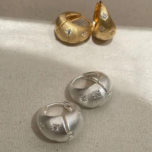 Elegant brushed metal star zircon earrings in gold and silver finish on textured fabric