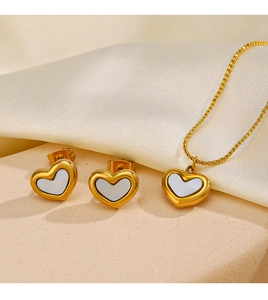 Detailed shot of golden shell heart necklace and stud earrings set on beige silk