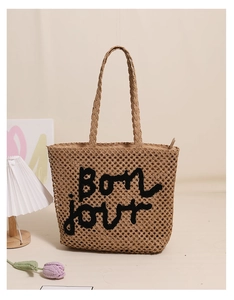 Detail of woven straw tote bag with black Bonjour embroidery and zipper closure