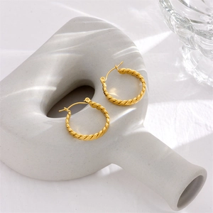 Pair of thick twisted gold hoop earrings on a white minimalist ceramic display stand