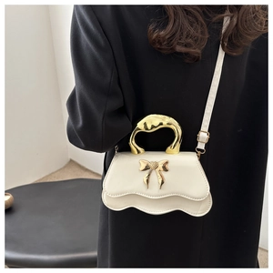 Close-up of white wavy handbag with gold bow clasp and irregular metal handle