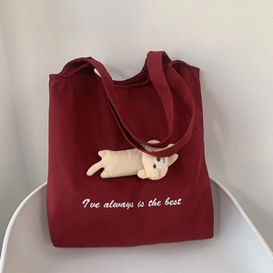 Detail of burgundy canvas tote bag featuring a cute 3D plush cat charm and white typography