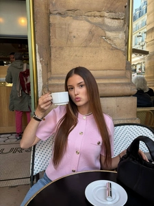 Dettaglio del cardigan rosa a maniche corte con bottoni dorati in una via francese