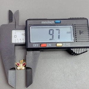 Macro view showing dimensions of a gold butterfly pendant with red stones using a digital caliper