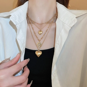 Detailed view of layered gold heart and globe pendant necklace on a female model