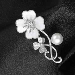 Macro shot of silver shell clover brooch with white pearl and zircon on black fabric