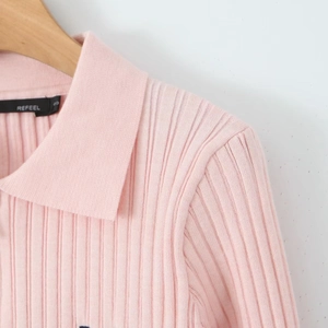 Détail du pull polo en maille côtelée rose montrant l'étiquette REFEEL et le col fini