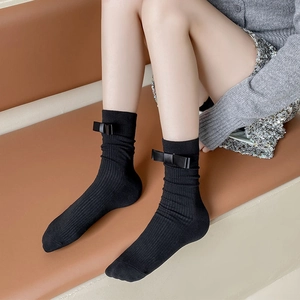 Detail of black ribbed mid-calf socks with bow tie decoration on a brown leather sofa