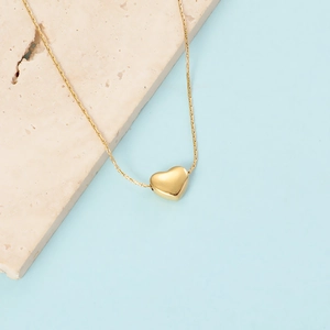 Flat lay of a gold heart pendant necklace on a beige stone and light blue background