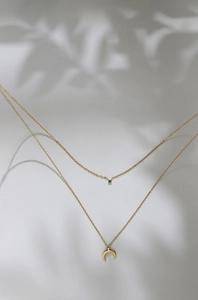 Detailed view of double-layer gold moon necklace with green gemstone and leaf shadows