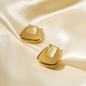 Macro shot of gold-finished U-shaped earrings on elegant golden silk fabric background