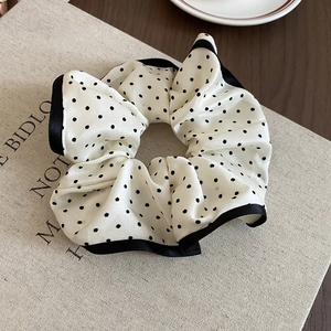 Polka dot silk fabric scrunchie with black trim on a textured book surface
