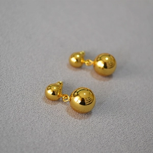 Vista macro di orecchini minimalisti a doppia sfera placcati in oro su sfondo grigio