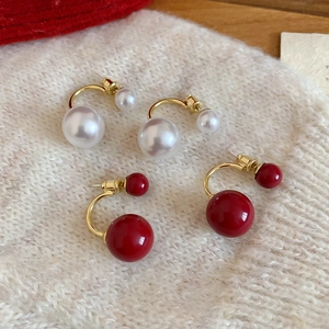 Dettaglio di orecchini a C placcati oro 14k con perle rosse e bianche su tessuto a maglia