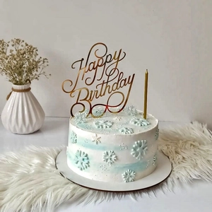 Golden acrylic Happy Birthday cake topper on a blue and white snowflake cake