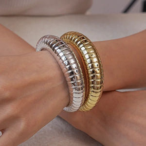 Detail shot of stacked gold and silver ribbed tubogas bracelets on a model's wrist