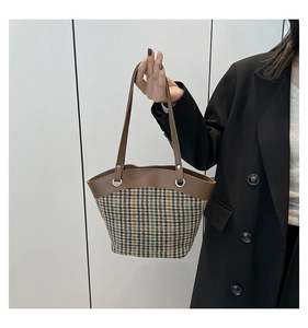 Detail of vintage plaid canvas bucket bag with leather handle held by a model