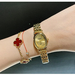 Detail of a gold quartz watch with an oval face and chain band worn on a model wrist