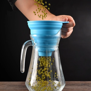 Blue collapsible silicone funnel pouring green beans into a glass jar kitchen detail