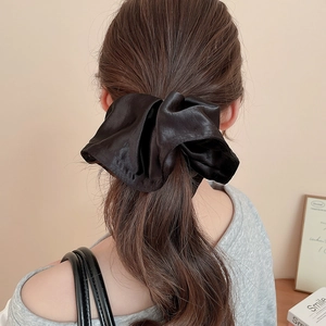 Close-up of a large black satin scrunchie with elegant folds on a model's hair