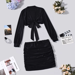 Flat lay of black satin tie-front top and ruched mini skirt with fashion accessories