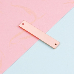 Macro shot of rose gold rectangular connector charm on pink and blue background
