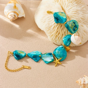Turquoise bead and gold chain bracelet with starfish charms on a beach theme background