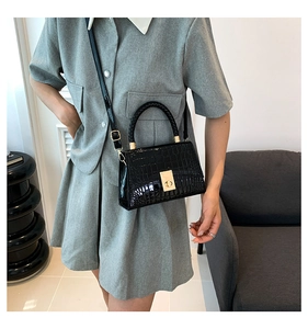 Detail of crocodile embossed crossbody bag with golden square lock and woven handle
