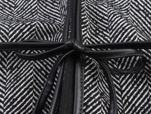 Detailed close-up of black and white herringbone tweed fabric with a leather bow tie detail