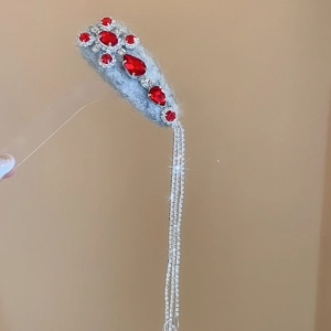 Detail of grey velvet hair clip with red waterdrop gems and long silver chain tassels