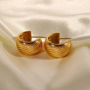 Elegant gold C-shaped twisted metal hoop earrings resting on beige satin fabric