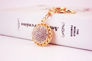 Close-up of golden rhinestone ball keychain with lobster clasp on a white book prop