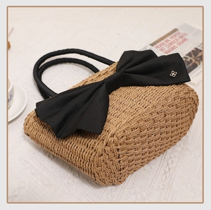 Detail of hand-woven straw bag with a large black bow and gold clover emblem