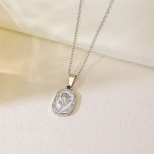 Macro view of oval rose relief pendant with white pearl base on a silver steel chain