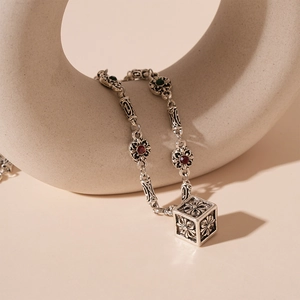 Detail of silver hollow cube necklace with floral cross engraving and gemstones