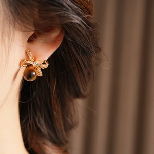 Close-up of gold bow earrings with clear zircons and brown tiger eye stone on model