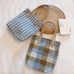 Detailed close-up of plaid canvas tote bags with brown leather handles and metal rivets