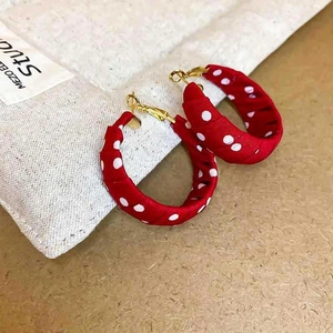 Detailed view of red polka dot fabric wrapped C-shaped hoop earrings on beige background