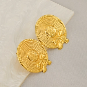 Golden sun hat earrings with bow detail on a white marble and gray textured base