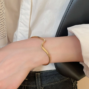 Close-up of golden irregular wavy cuff bracelet styled with white shirt and black bag