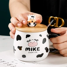 Close-up of hands holding a cow pattern ceramic mug with wooden lid and cow figurine