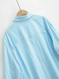 Detail view of light blue shirt collar and back pleat design on a wooden hanger